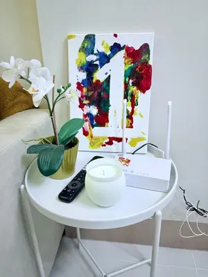 a white table with a painting and a remote control at MOA Staycation Haven Cozy 1BR Retreat with Balcony at Shore 3 in Manila