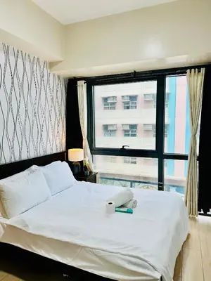 a bedroom with a white bed with a window at Comfy 1BR Across International Airport in Manila