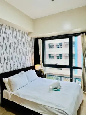 a bedroom with a white bed with a window at Comfy 1BR Across International Airport in Manila