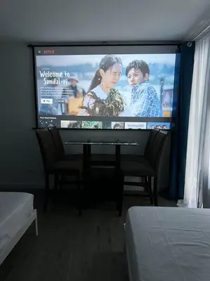 a flat screen tv with a movie on it at Studio w projector Wifi Netflix and pool access in ADB Tower Ortigas CBD in Manila