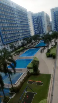 a view of a large swimming pool with palm trees and buildings at Sea res moa by Elsie D in Manila