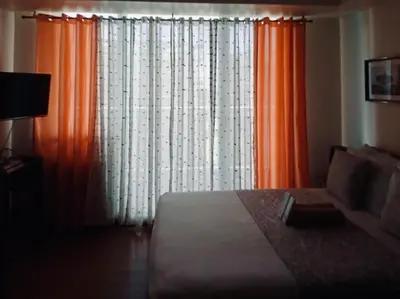 a bedroom with a bed and a window with orange curtains at Spacious 1Bedroom Condotel Resort in Manila
