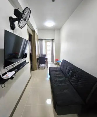 a living room with a black couch and a flat screen tv at Coast Residences - 1 Bedroom with Balcony near PICC, WTC, Star City & MOA in Manila