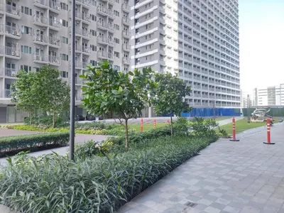 a walkway with trees and plants in front of tall buildings at FAME Bedroom in Manila