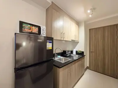 a kitchen with a black refrigerator and wooden cabinets at 1BR Condotel with Balcony at FAME Residences #FM57 in Manila