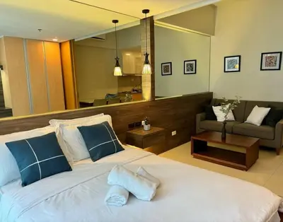 a bedroom with a large bed and a living room at Comfy 1BR At Uptown BGC in Manila
