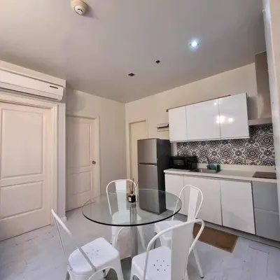 a kitchen with a glass table and white chairs at Cozy Two Bedroom Flat in The Gramercy Residences in Manila