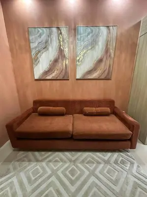a brown couch in a living room with three paintings at Cozy orange room at shore in Manila