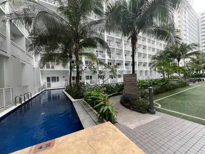 a swimming pool in front of a building with palm trees at Shore Family Suite 2 Beds WiFi TV Netflix Near MOA 9120 in Manila