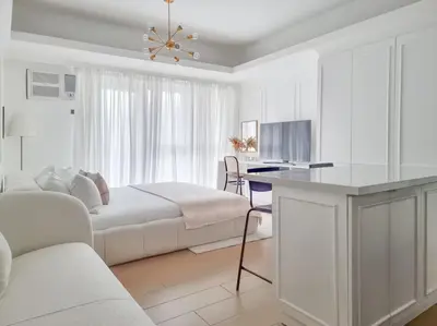 a white living room with a bed and a desk at King Bed, Washer, Air Dry, Sauna, Gym & Pool Access, FAST Wi-Fi, Elegant Studio, Near Venice Grand Canal Mall, Walking Distance Britsh Embassy, 5 min drive to BGC, 10 min drive to Manila Airport NAIA 3 in Manila