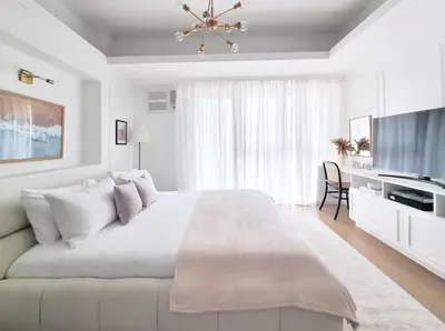 a white bedroom with a large bed and a television at King Bed, Washer, Air Dry, Sauna, Gym & Pool Access, FAST Wi-Fi, Elegant Studio, Near Venice Grand Canal Mall, Walking Distance Britsh Embassy, 5 min drive to BGC, 10 min drive to Manila Airport NAIA 3 in Manila