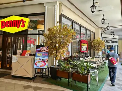 a man walking past a store with tables and chairs at King Bed, Washer, Air Dry, Sauna, Gym & Pool Access, FAST Wi-Fi, Elegant Studio, Near Venice Grand Canal Mall, Walking Distance Britsh Embassy, 5 min drive to BGC, 10 min drive to Manila Airport NAIA 3 in Manila