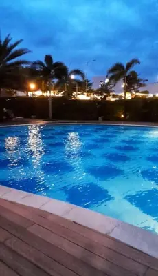a large blue swimming pool at night with palm trees at South Residences, Las Piñas in Manila