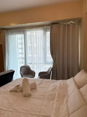 a bedroom with a white bed with two chairs and a window at Condotel near NAIA T3 Airport in Manila