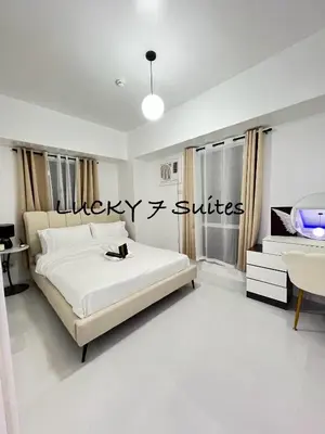 a white bedroom with a bed and a desk at LUCKY 7 Suites in Manila