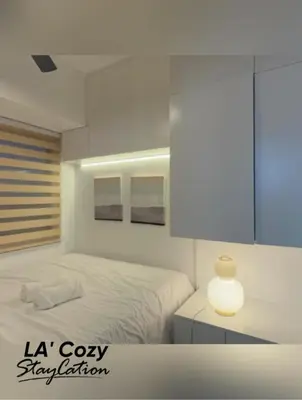 a white bedroom with a white bed and a lamp at Flat in Pasay-Coast Residences in Manila