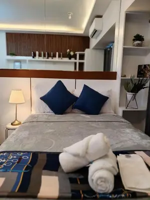 a bedroom with a bed with blue pillows and towels at Affordable Modern Studio with Netflix WiFi Balcony in Air Residences in Manila