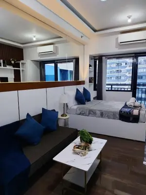 a living room with a couch and a bed with blue pillows at Affordable Modern Studio with Netflix WiFi Balcony in Air Residences in Manila