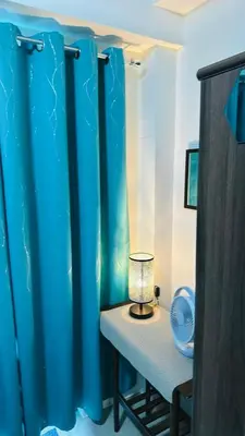 a lamp on a table in a room with blue curtains at Homey Staycation at MOA Complex in Manila