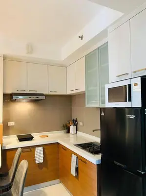 a kitchen with a black refrigerator and wooden cabinets at HIGHLY RECOMMENDED La Nooq MNL - Cozy 1BR Skyline view in Mandaluyong in Manila