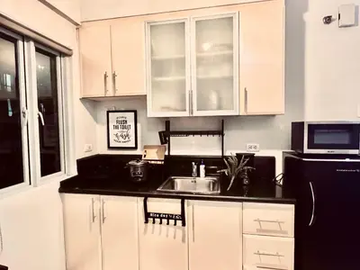 a kitchen with white cabinets and a sink and a microwave at Cozy Home in BGC McKinley B2 in Manila