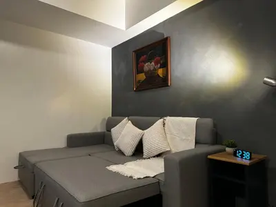 a couch in a living room with a clock on the wall at 1BR Stay near NAIA Terminal 3 via Runway Manila in Manila