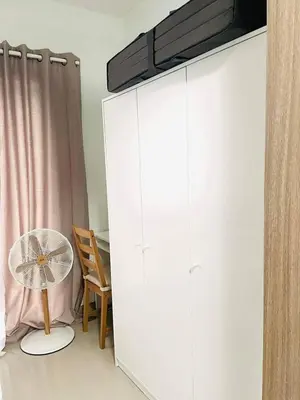 a white cabinet with a fan next to a chair at Pasay Condo near MOA, NAIA, CBD and Casinos in Manila