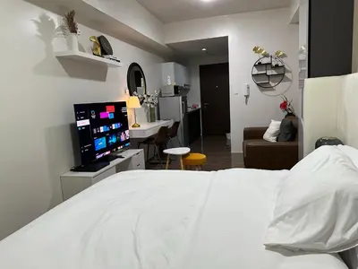 a bedroom with a white bed and a living room at King-size Bed Makati Condo in Manila
