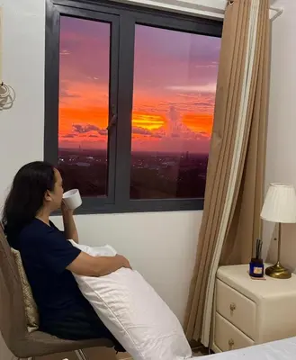 a woman sitting in a chair drinking a cup of coffee looking out a window at Green 2 SMDC - STUDIO TYPE Condo - Gems Suite Staycation in Dasmariñas