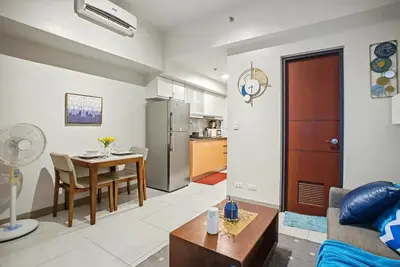 a living room with a table and a kitchen at BGC High Rise, Uptown Mall Connector, 5G WiFi, Pool, Ste 15 in Manila