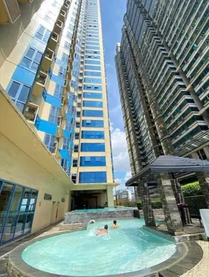 two people in a swimming pool in front of a tall building at Urban haven Family&Barkada room in Manila