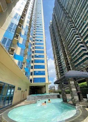 two people in a swimming pool in front of a tall building at Studio type unit 1, infront of US Embassy Manila in Manila