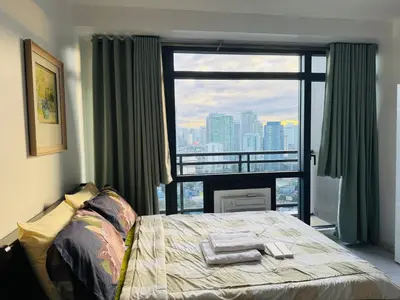 a bedroom with a bed and a large window at Gramercy Residences Studio With Balcony City View in Manila