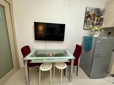 a glass table with two chairs and a tv on a wall at Staycation Near Moa by Jen in Manila