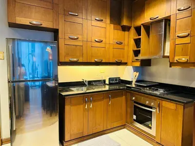 a kitchen with wooden cabinets and a refrigerator at Cozy, Spacious 1 Bedroom Condo, reach St Lukes BGC by foot in Manila