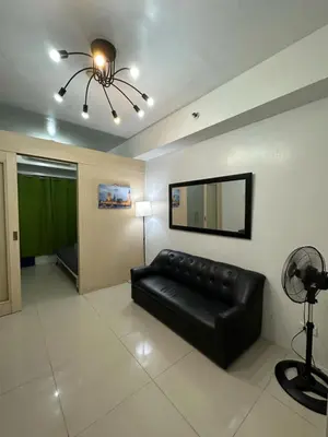a living room with a black leather couch and a television at MOA Complex Staycation in Manila
