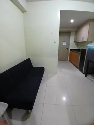 a living room with a black couch and a kitchen at Breeze Residences in Manila