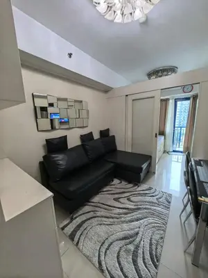 a living room with a black couch and a rug at Athalia's Pad at Sea Residences in Manila