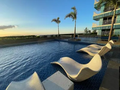 a swimming pool with white chairs and a building at Stunning 2BR across Okada Manila with Sunset View in Manila