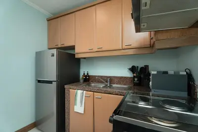 a kitchen with wooden cabinets and a stainless steel refrigerator at Studio in Greenbelt Makati with Fiber WiFi & Free Pool Access in Manila