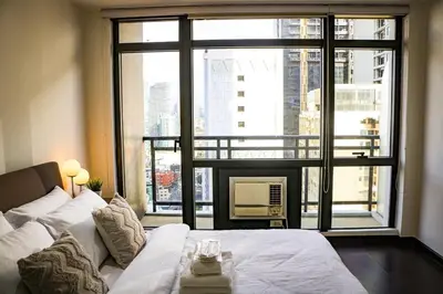 a living room with a white couch and a large window at Snug Stay in Gramercy Makati with City Skyline View! in Manila