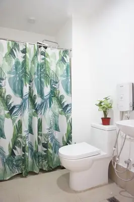 a bathroom with a toilet and a green and white shower curtain at Modern Tropical Home In The Heart of Quezon City in Manila