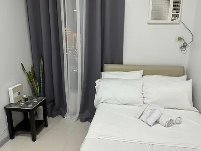 a bed with white pillows and a night stand next to a window at Eve's Den in Manila