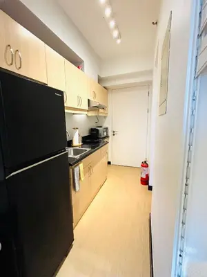 a kitchen with a black refrigerator and wooden cabinets at Free Car Parking - Sheridan North 1BR Apt near BGC in Manila
