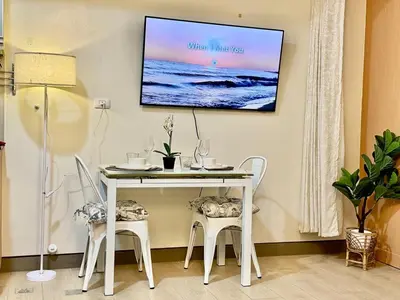 a white table and chairs with a tv on a wall at Cozy Home at Venice Luxury BGC in Manila