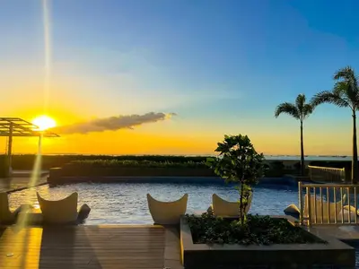 a sunset over a pool with chairs and palm trees at Spacious 3BR condo across Okada Manila and Solaire in Manila