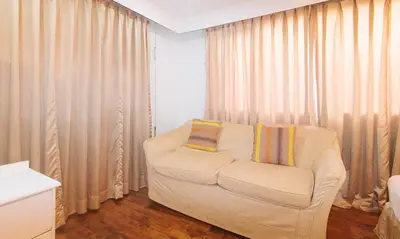 a living room with a white chair and curtains at Comfy Inn Manila Kalaw by RedDoorz in Manila