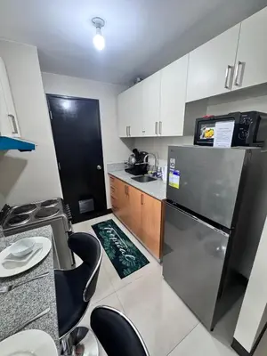 a small kitchen with a refrigerator and some chairs at 2 Bedroom with Balcony in Manila