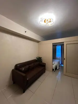 a living room with a brown leather couch and a bedroom at Sea Residences MOA Pasay City- Kirk in Manila