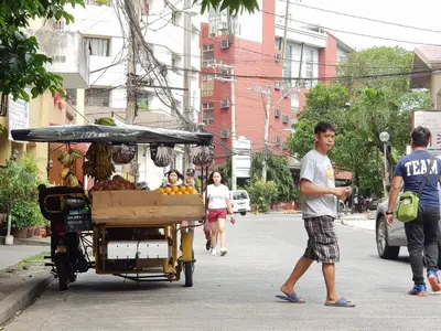 a man walking down a street with a fruit cart at Delet TEA in Manila